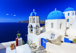  Weißgetünchte Häuser und Kirchen mit ikonischen blauen Kuppeln machen Santorini zu einem weltbekannten Postkartenmotiv. 