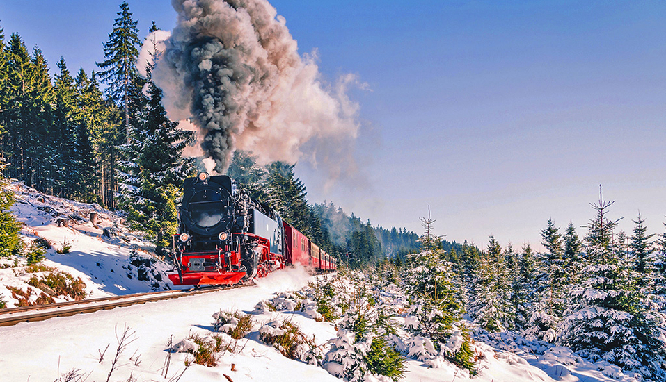 Die Brockenbahn schlängelt sich in leuchtendem Rot durch die weiße Winterlandschaft.