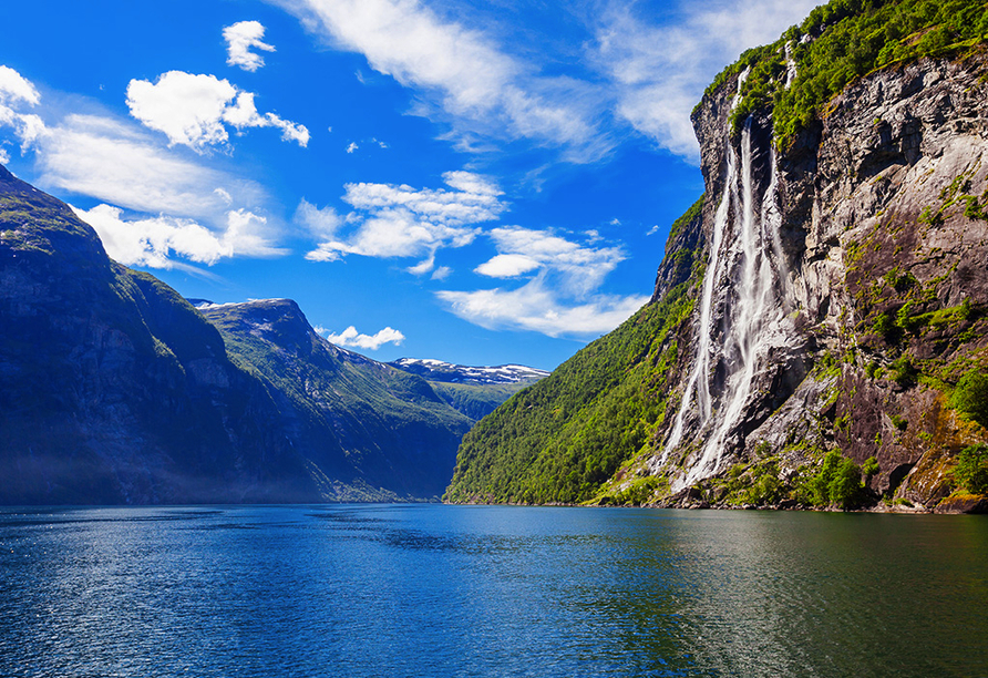 Der UNESCO-geschützte Geirangerfjord ist umgeben von majestätischen, schneebedeckten Berggipfeln, wilden Wasserfällen und grünen Tälern.