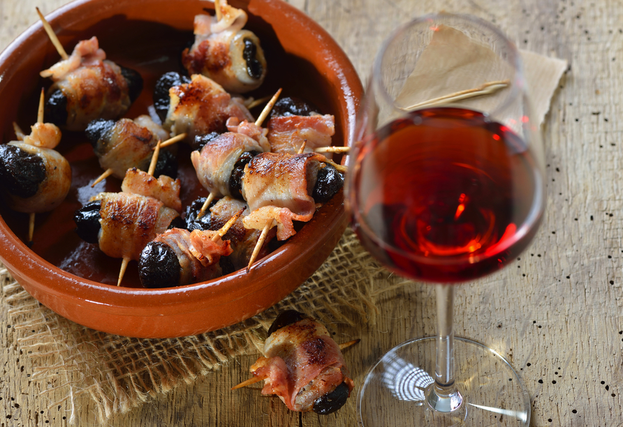 Probieren Sie leckere Tapas: Getrocknete Pflaumen in Speck gerollt und gebraten, dazu ein Glas Old Tawny Portwein.