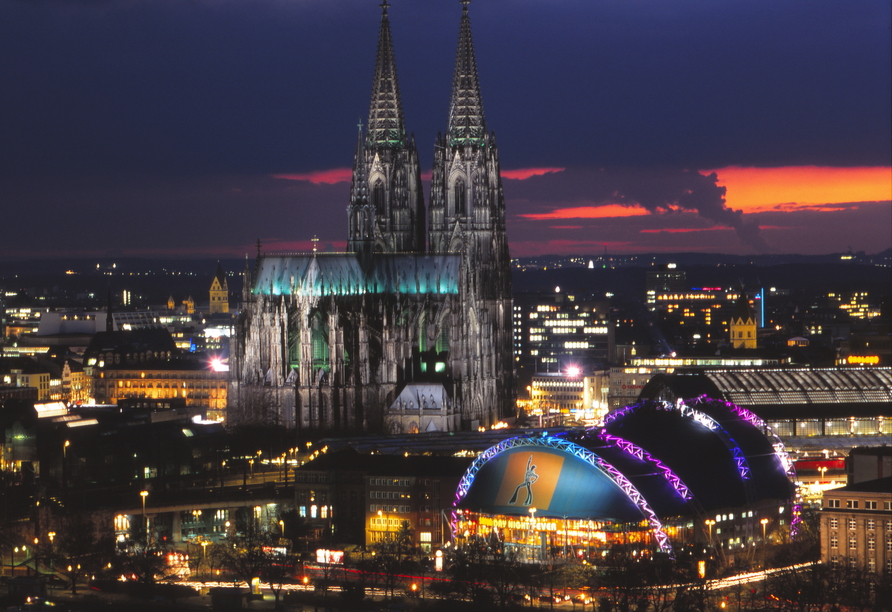 Köln am Abend mit dem Dom und dem Musical Dome, in dem MOULIN ROUGE! Das Musical aufgeführt wird.