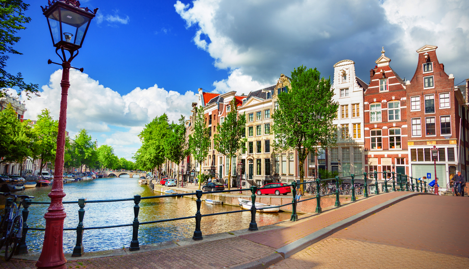 Schlendern Sie in Amsterdam entlang schöner Grachten mit pittoresken Häusern im Hintergrund.