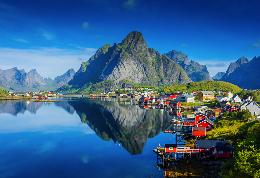 Das Dorf Reine befindet sich in den Lofoten und glänzt mit typisch roten Fischerhütten vor der Kulisse majestätischer Berge.