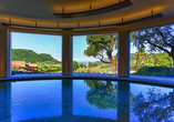 Entspannen Sie im Hallenbad des Wellnessbereichs mit atemberaubendem Ausblick auf den Gardasee.