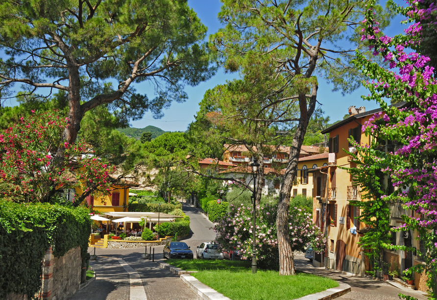 Blühende Sträucher und schattige Bäume säumen die charmanten Straßen von Gardone Riviera.