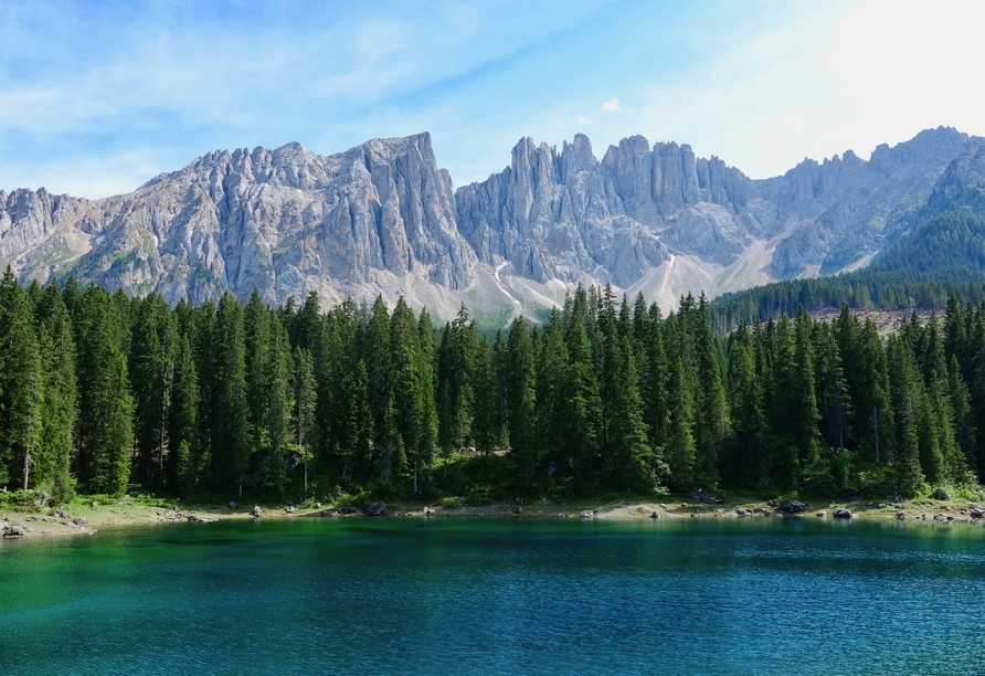 Berge und Bäume spiegeln sich im grünen Karersee in Südtirol.