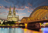 Der Kölner Dom und die Lichter der Stadt spiegeln sich im Rhein zur Dämmerung.