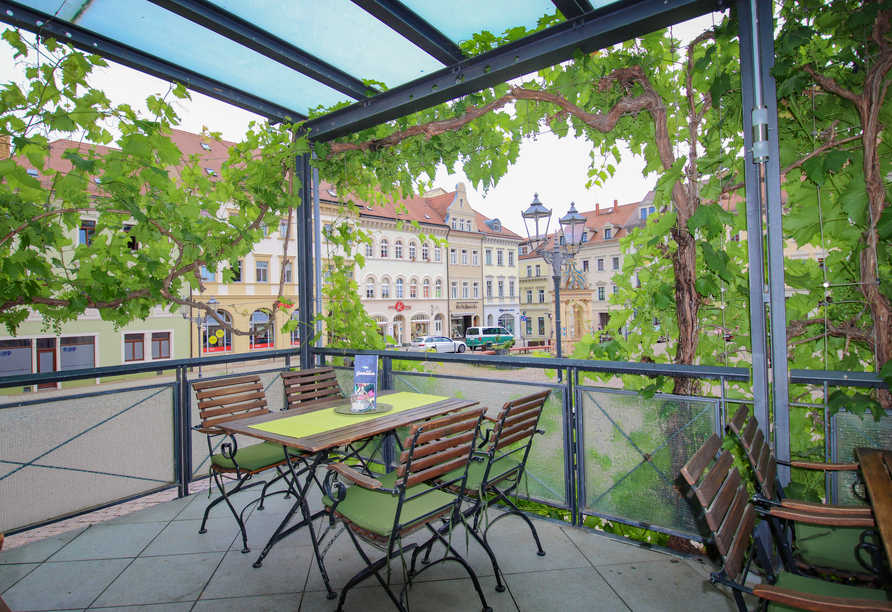Umgeben von Weinreben sitzen Sie auf der Terrasse.