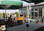 Entspannen Sie auf der sonnigen Hotelterrasse mit kühlen Getränken, bequemen Sitzplätzen und sommerlicher Atmosphäre.