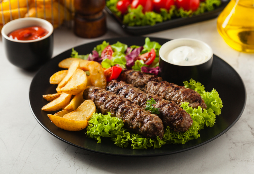 Herzhaft, aromatisch und einfach köstlich – Cevapcici mit knusprigen Kartoffeln und frischem Salat bringen den Geschmack des Balkans auf den Teller.
