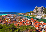 Vor der Kulisse markanter Felsen schmiegt sich die Altstadt von Omiš an das türkis schimmernde Meer und den smaragdgrünen Fluss Cetina, ein Panorama voller mediterraner Lebensfreude.