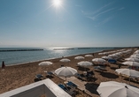 Sonniger Strand mit Liegen und Schirmen direkt am glitzernden Meer