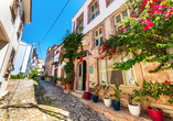 Spazieren Sie durch die Gassen von Cunda und entdecken Sie historische Häuser, blühende Pflanzen und mediterranes Flair.